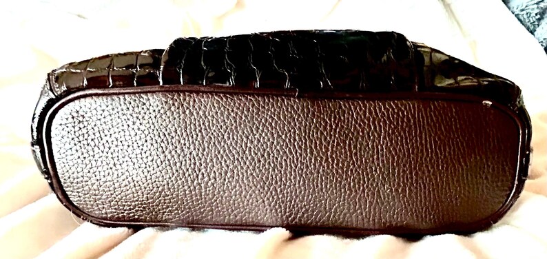 May include: A brown leather handbag with a crocodile-embossed design. The bag has a smooth, textured bottom.