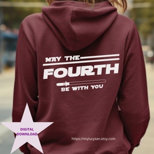 Puede incluir: Una sudadera con capucha granate con texto blanco que dice "MAY THE FOURTH BE WITH YOU" y un gráfico de sable de luz. La sudadera con capucha también tiene un gráfico de estrella de descarga digital y una dirección de sitio web.