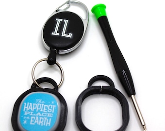 Puede incluir: Un conjunto de accesorios que incluye un llavero negro con las letras "IL", un llavero con el texto "THE HAPPIEST PLACE ON EARTH", un anillo negro y un pequeño destornillador con la parte superior verde.