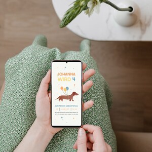 Puede incluir: Un tel&eacute;fono inteligente que muestra una invitaci&oacute;n de cumplea&ntilde;os para el 4&ordm; cumplea&ntilde;os de Johanna. La invitaci&oacute;n presenta un dachshund de dibujos animados con globos y el texto "Johanna wird 4". La invitaci&oacute;n tambi&eacute;n incluye la fecha y la hora de la fiesta, as&iacute; como la direcci&oacute;n.