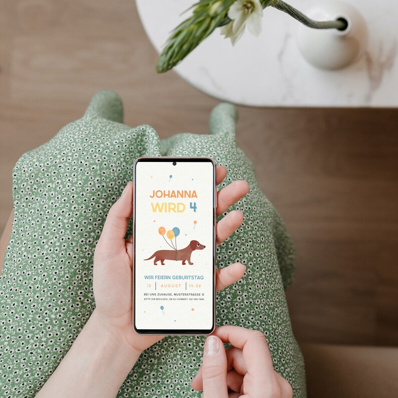 Puede incluir: Un tel&eacute;fono inteligente que muestra una invitaci&oacute;n de cumplea&ntilde;os para el 4&ordm; cumplea&ntilde;os de Johanna. La invitaci&oacute;n presenta un dachshund de dibujos animados con globos y el texto "Johanna wird 4". La invitaci&oacute;n tambi&eacute;n incluye la fecha y la hora de la fiesta, as&iacute; como la direcci&oacute;n.
