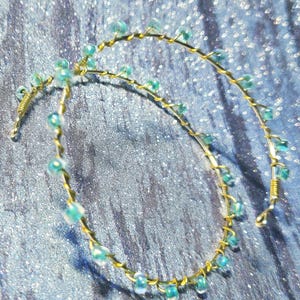 May include: A delicate, handcrafted headpiece featuring a gold-colored wire base adorned with small, light blue beads. The beads are evenly spaced along the wire, creating a subtle, elegant design. The headpiece is likely for special occasions.
