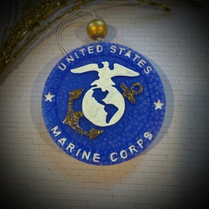 May include: A blue and gold round ornament with the words "United States Marine Corps" and the Marine Corps emblem.