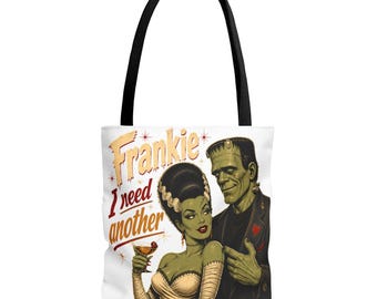 May include: A white tote bag with black handles featuring a graphic illustration of Frankenstein's monster and his bride. The text reads Frankie I need another. The bride holds a cocktail glass, and the monster wears a dark jacket with a red heart.