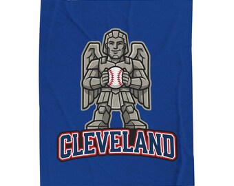 May include: A royal blue blanket featuring a graphic of a gray stone-like winged guardian figure holding a white baseball with red stitching. Below the figure, the word CLEVELAND is printed in bold blue letters with a red and white outline.