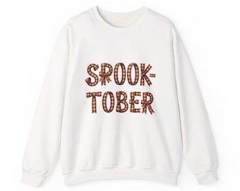 May include: A white crewneck sweatshirt featuring the text "SPOOK-TOBER" printed on the front. The letters are designed to look like ribbons tied into bows, featuring a red, orange, and black plaid pattern throughout the graphic design.