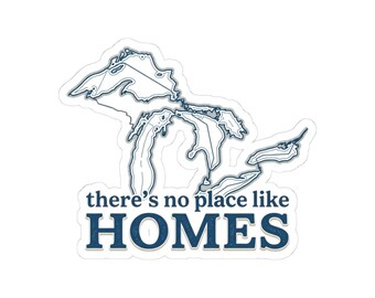 May include: A die-cut sticker featuring a dark blue outline map of the Great Lakes. Below the map, the text reads there's no place like HOMES in a bold, dark blue serif font. The design is set against a clean white background with a thin border.