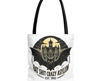 May include: A white tote bag with black handles featuring a circular graphic of a bat in front of a gothic asylum building under a full moon. The text reads BAT SHIT CRAZY ASYLUM EST. 1982 in a bold, dark font centered below the bat illustration.