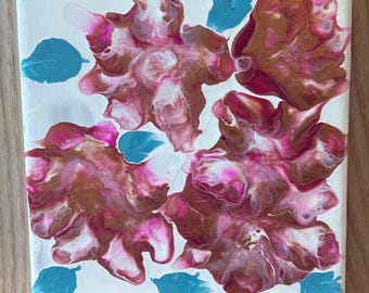 May include: A square ceramic tile featuring an abstract fluid acrylic pour design. The surface displays three large, organic floral-like shapes in shades of metallic gold, magenta, and white, accented by small, solid turquoise leaf-like shapes.