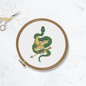 May include: A green snake with a gold bird and arrow embroidered on a white fabric in a wooden embroidery hoop.