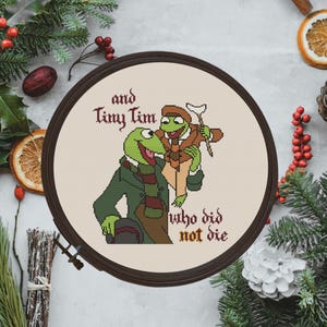 Puede incluir: Un bastidor de punto de cruz con Kermit la Rana y Tiny Tim de Los Muppets, con el texto "and Tiny Tim who did not die". Los personajes visten ropa de invierno. El bastidor está rodeado de vegetación festiva.