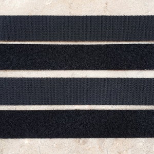 May include: Four black hook and loop fastener strips are arranged horizontally. The strips have different textures, with some having a looped surface and others a hooked surface. The strips are rectangular and appear to be made of fabric.