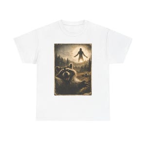 Könnte beinhalten: Weißes T-Shirt mit einem Grafikdesign im Vintage-Stil. Die Grafik zeigt einen lächelnden Waschbären in einer Waldszene, mit einer Silhouette einer Figur im Hintergrund. Das Design hat einen Sepia-Ton und wirkt retro.