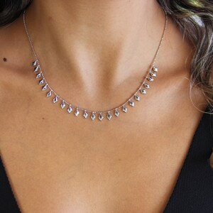 May include: A silver necklace with a delicate chain and diamond-shaped pendants hanging from it. The necklace is worn by a person with long brown hair.