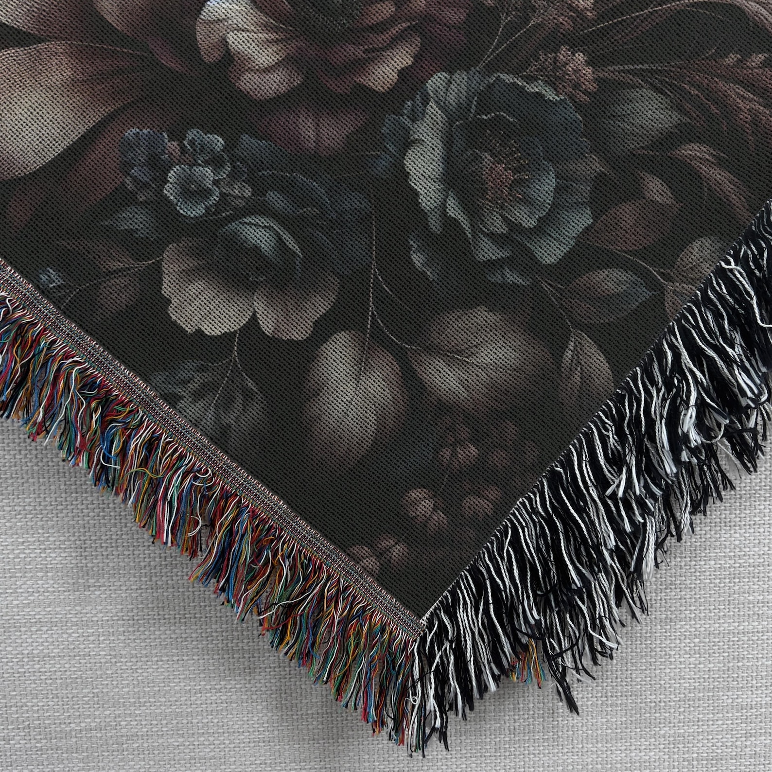 Close-up of corner detail on black woven floral throw blanket with multicolor fringe and muted baroque-style flower print