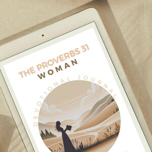 May include: A digital tablet showing a devotional journal cover. The cover has the text "THE PROVERBS 31 WOMAN" and a circular illustration of a woman in a landscape. The tablet is on a neutral surface with a woven placemat.