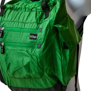May include: A green backpack with black straps and zips. The backpack features multiple compartments and the brand name "böken" is visible. It appears to be made of a lightweight, possibly water-resistant material.