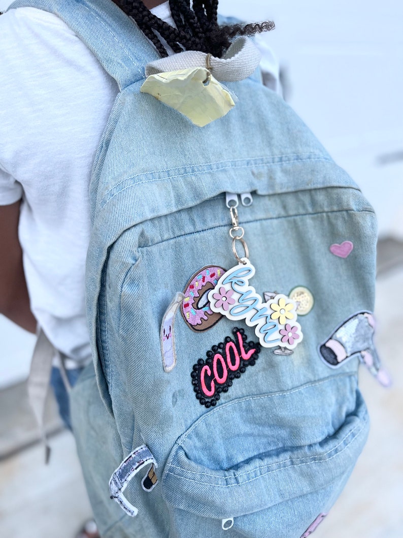 May include: A light blue denim backpack with various colourful patches, including a donut, a flower, a drink, and the word "cool".