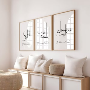 Puede incluir: Tres impresiones enmarcadas con caligrafía árabe en negro sobre fondo blanco. Las impresiones están en marcos dorados y presentan las palabras "Allahu Akbar", "Alhamdulillah" y "Subhanallah".