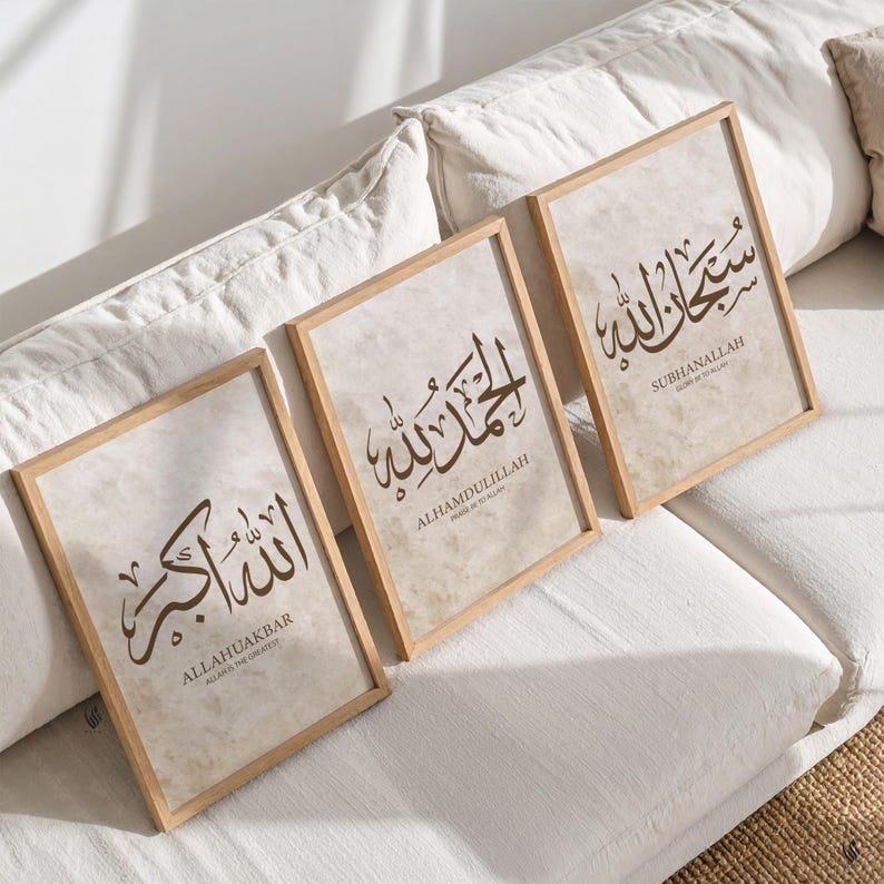 May include: Three framed art prints with Islamic calligraphy in brown script on a beige background. The wooden frames are rectangular. The prints feature the phrases: ALLAHUAKBAR, ALHAMDULILLAH, and SUBHANALLAH, with English translations below.