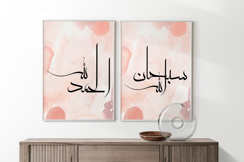 May include: Two framed prints with a watercolor background in shades of pink and white. The prints feature Arabic calligraphy in black ink. The text on the left print reads "Alhamdulillah" and the text on the right print reads "Masha'Allah".