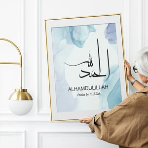 May include: A framed print with a blue watercolor background and black calligraphy that reads "Alhamdulillah" with the English translation "Praise be to Allah".