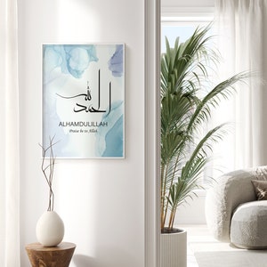 May include: A framed print with a blue watercolor background and the Arabic calligraphy for "Alhamdulillah" in black. The text "Praise be to Allah" is written below the calligraphy.