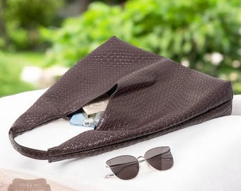 May include: A brown woven leather tote bag with a woven pattern. The bag is lying on a white surface with sunglasses next to it.