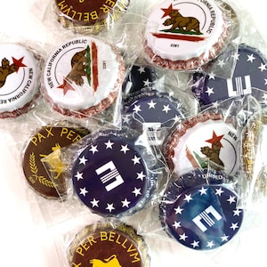 May include: A collection of 10 bottle caps with various designs. The bottle caps are mostly brown, blue, and white with gold accents. Some of the bottle caps feature a bull, a bear, and a star design. The text "PAX PER BELLVM" is visible on some of the bottle caps.