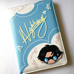 Könnte beinhalten: Ein hellblaues Portemonnaie mit einer Cartoon-Illustration eines Charakters mit schwarzen Haaren und blauen Augen. Das Portemonnaie hat ein Wolken- und Stern-Design mit dem Wort "Lightning" in gelber Schrift.