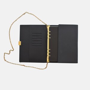 May include: Black organizer with a gold chain strap. The open organizer reveals a gold-colored binder mechanism and card slots. The exterior features a gold clasp closure.