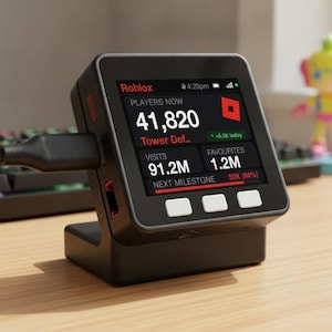 May include: A black square digital display device on a stand, showing Roblox game statistics including 41,820 players, 91.2M visits, and 1.2M favorites. The screen features a red logo, white text, and three white buttons below the display screen.