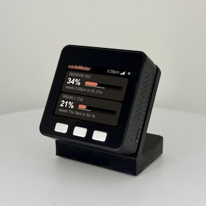 K&ouml;nnte beinhalten: Ein schwarzes digitales Ger&auml;t, das Daten auf einem Bildschirm anzeigt und auf einem schwarzen St&auml;nder montiert ist. Der Bildschirm zeigt den Text "codeMeter" und Datenbalken mit Prozentangaben und Reset-Zeiten. Das Ger&auml;t hat drei wei&szlig;e Tasten.