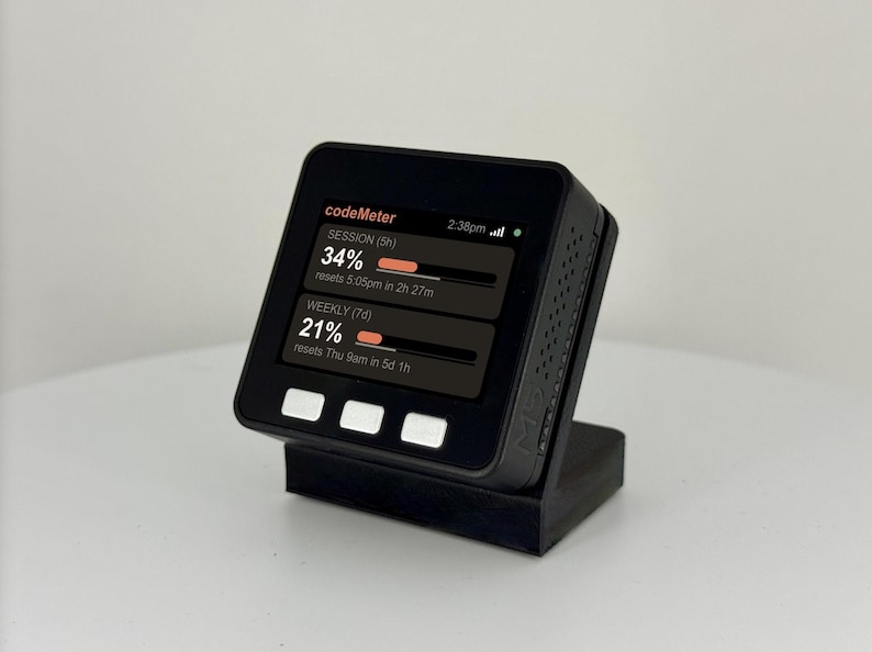 K&ouml;nnte beinhalten: Ein schwarzes digitales Ger&auml;t, das Daten auf einem Bildschirm anzeigt und auf einem schwarzen St&auml;nder montiert ist. Der Bildschirm zeigt den Text "codeMeter" und Datenbalken mit Prozentangaben und Reset-Zeiten. Das Ger&auml;t hat drei wei&szlig;e Tasten.