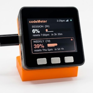K&ouml;nnte beinhalten: Ein schwarzes und orangefarbenes digitales Ger&auml;t mit der Aufschrift "codeMeter" auf dem Bildschirm. Der Bildschirm zeigt Fortschrittsbalken f&uuml;r Sitzungen und Wochen an. Das Ger&auml;t ist mit einem schwarzen Kabel angeschlossen und steht auf einem orangefarbenen St&auml;nder.