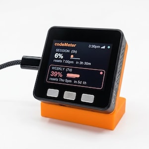 K&ouml;nnte beinhalten: Ein schwarzes und orangefarbenes digitales Ger&auml;t mit einem Bildschirm, der Daten anzeigt, darunter der Text "codeMeter", "SESSION" und "WEEKLY". Das Ger&auml;t ist angeschlossen und ruht auf einem orangefarbenen St&auml;nder. Der Bildschirm zeigt Prozents&auml;tze und die verbleibende Zeit an.