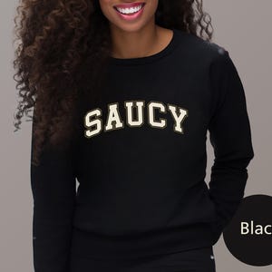 May include: Black sweatshirt with the word "SAUCY" printed in a white, collegiate-style font.