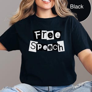 Può includere: T-shirt nero con la scritta "Free Speech" in un design in stile ritagliato. Il testo è bianco su sfondo nero. La maglietta è uno stile casual.