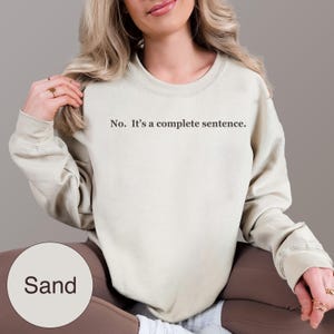 May include: Sand-colored sweatshirt with the text "No. It's a complete sentence." printed in black. The sweatshirt has a crew neck and long sleeves. The color is displayed in a label at the bottom left.