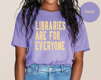 May include: A violet t-shirt with the text "LIBRARIES ARE FOR EVERYONE" in a light yellow color. The shirt is paired with blue jeans. A violet circle with the word "Violet" is in the upper right corner.