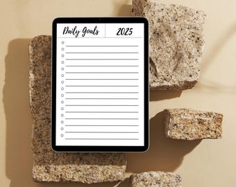 May include: A white digital tablet with a black screen displaying a daily goals list for 2025. The tablet is on a beige surface with several small, rough, brown rocks.