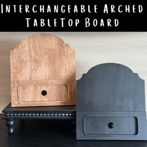 May include: Two interchangeable arched tabletop boards, one natural wood-toned and the other charcoal gray, are displayed. Each board has a drawer-like feature with a circular knob. The text "INTERCHANGEABLE ARCHED TABLETOP BOARD" is at the top.