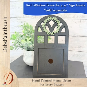 May include: A black arch window frame with a light green wreath, designed for 4.25-inch sign inserts. The frame is hand-painted home decor for every season.