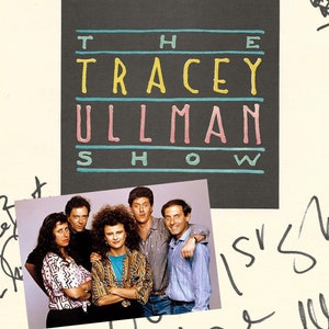 May include: A white sheet of paper with black text that reads "A thousand show journey begins with one script."  The text is followed by a handwritten signature.  Below the signature is a black and white image of a movie screen with the text "Gracie Films" on the screen.  Below the image is a black and white image of a group of people.  The text "The Tracey Ullman Show" is written in black and white letters.  The text "All the best, Love Tracey Ullman" is handwritten in black ink.  The text "Ditto-what they all said. Peace, Julia Kamm" is handwritten in black ink.  The text "20th Century Fox Television" is printed in black and white letters.