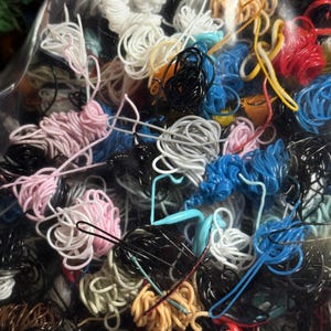 May include: A close-up of a variety of colorful and textured cords and wires. The cords are tangled together in a plastic bag.