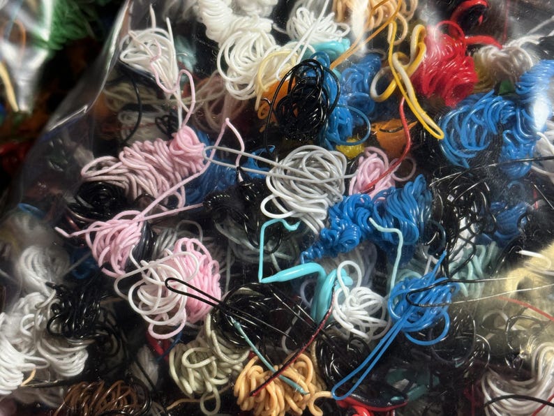 May include: A close-up of a variety of colorful and textured cords and wires. The cords are tangled together in a plastic bag.