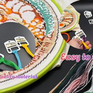 May include: A cross-stitch project in a green plastic embroidery hoop featuring a food-themed pattern with orange, teal, and black thread. White plastic thread organizers hold various colored embroidery floss including yellow, green, and blue.