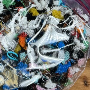 May include: A clear plastic bag filled with a variety of colorful and black string and wire. The bag is open and the contents are spilling out.