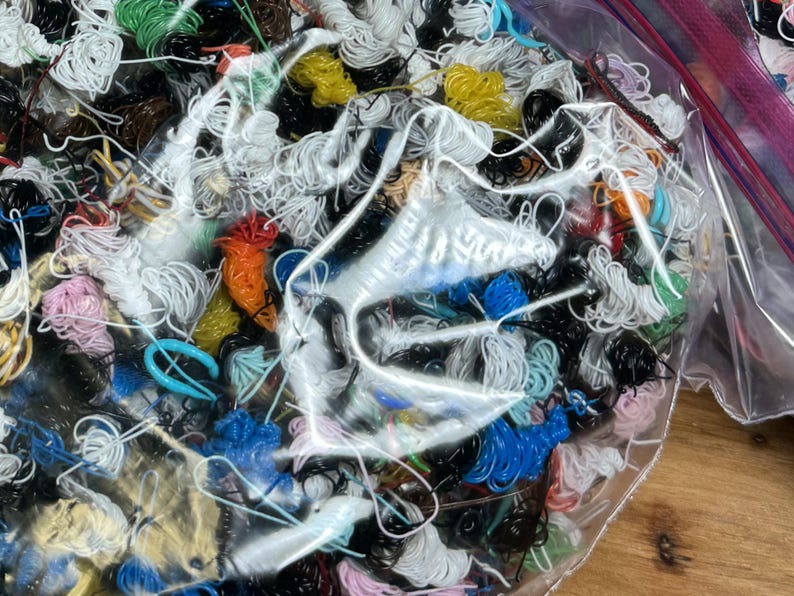 May include: A clear plastic bag filled with a variety of colorful and black string and wire. The bag is open and the contents are spilling out.