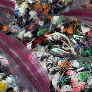 May include: Multiple clear plastic bags filled with colorful embroidery floss. The bags are partially open, revealing the various colors of thread.